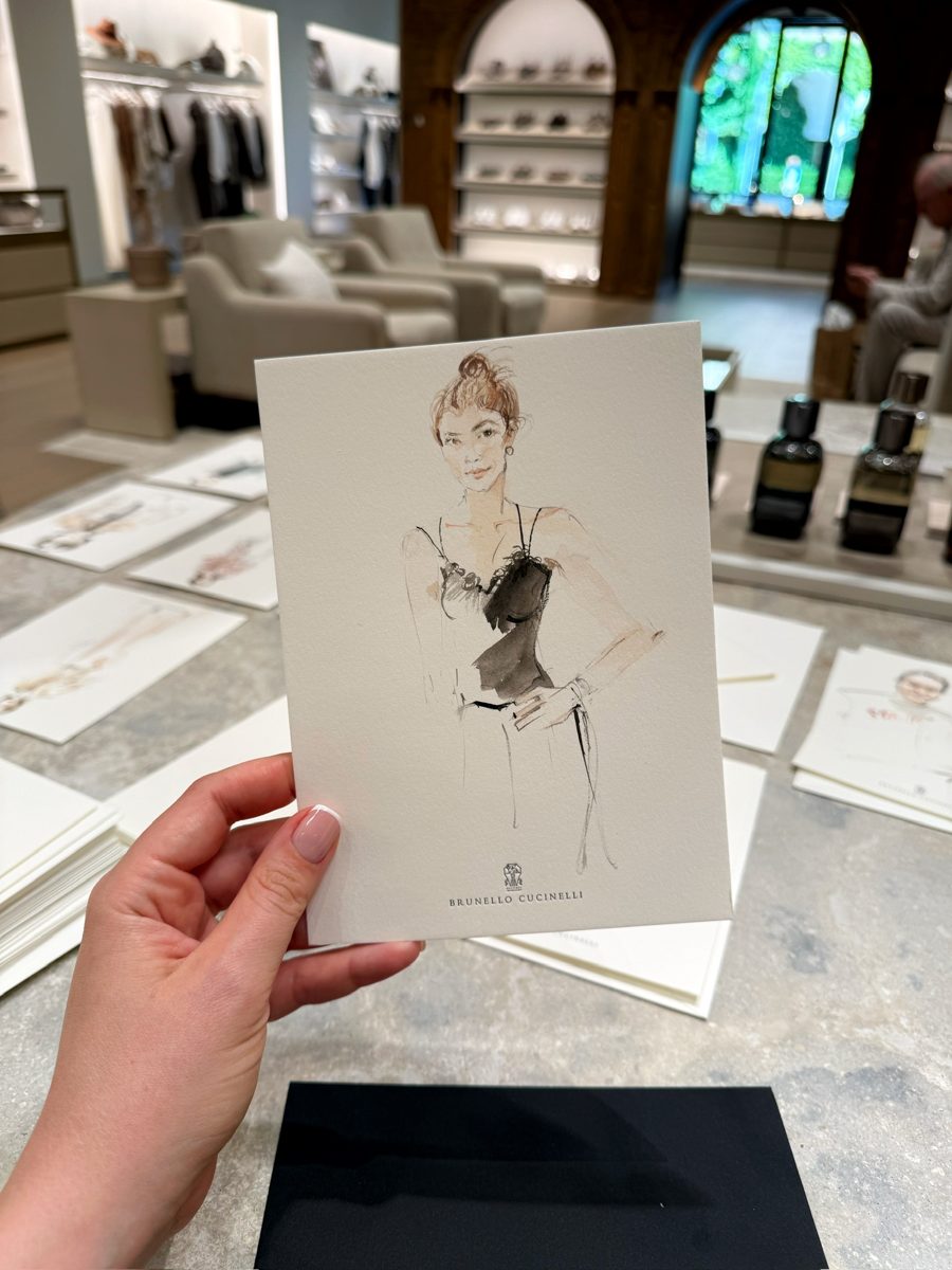 Live fashion portrait in ink and watercolour on a Brunello Cucinelli card, held up in the boutique